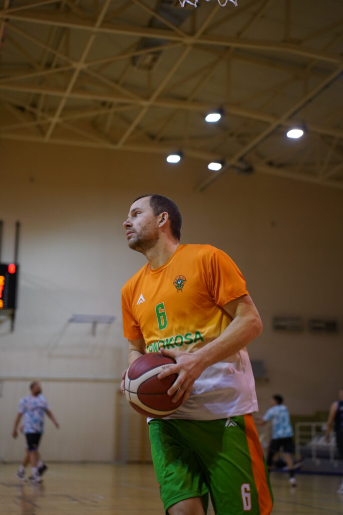 Muškarac u narandžastoj i beloj košarkaškoj majici drži košarkašku loptu.