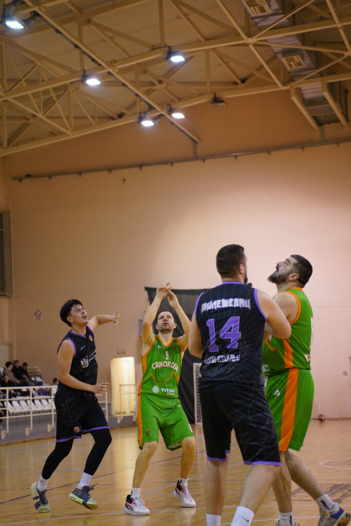 Košarkaši u zelenim i crnim uniformama na terenu, jedan igrač skače za šut.